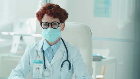 Portrait-of-Young-Female-Doctor-in-Mask-at-Desk-in-Clinic